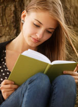 Woman sitting against tree trunk reading a book